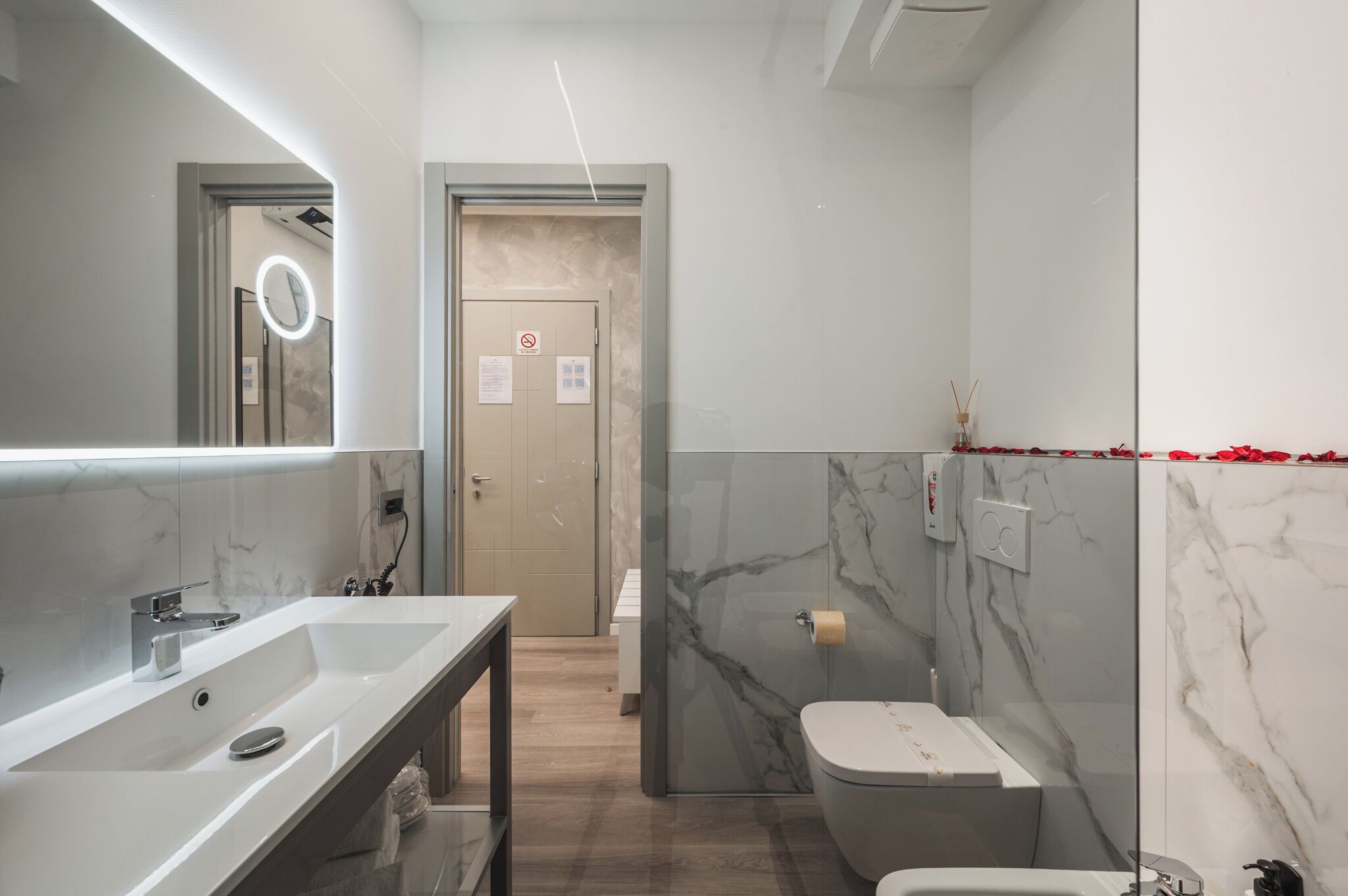 A modern bathroom with a large mirror, a sink, and a toilet.