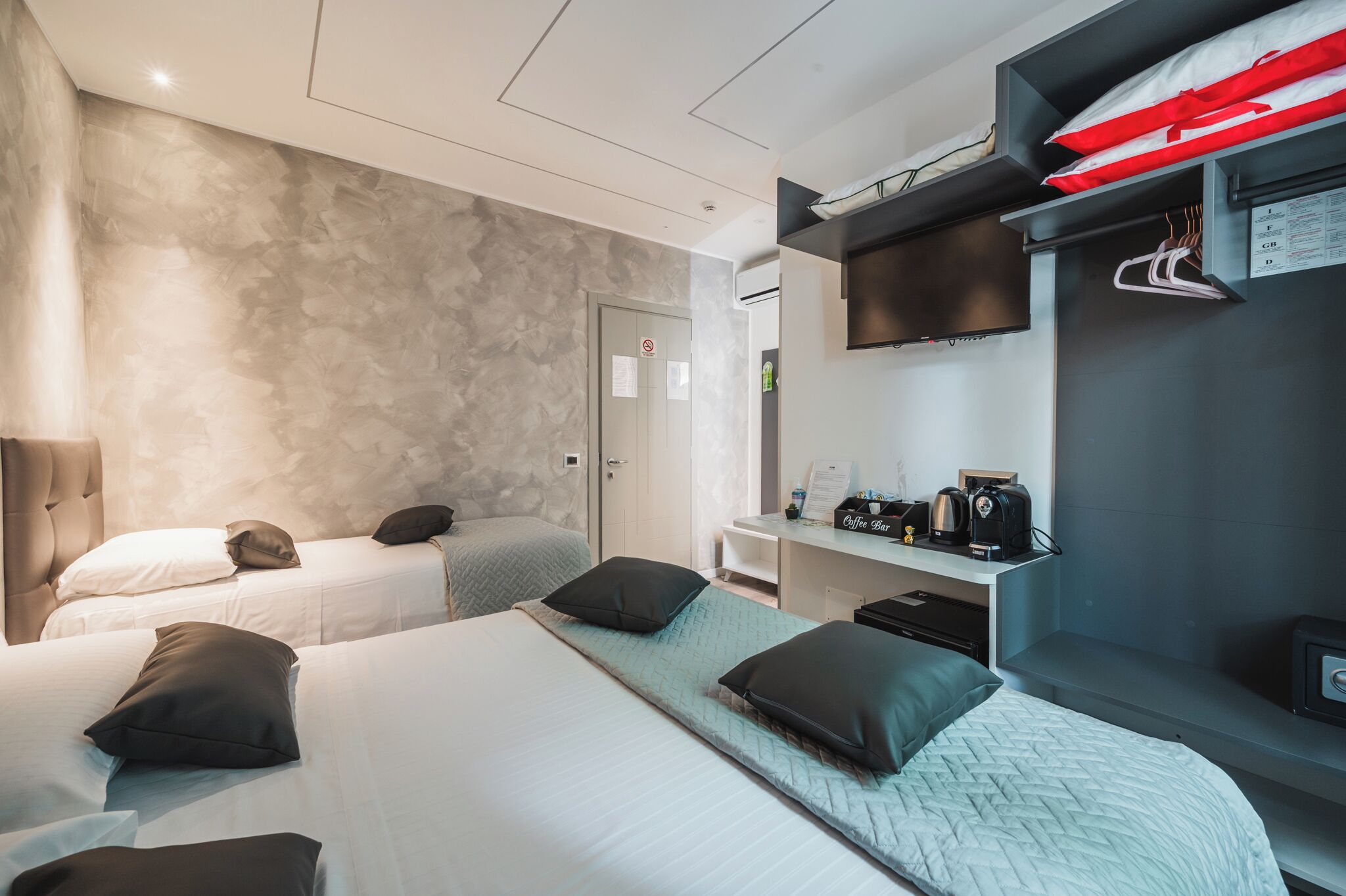Camera d'albergo con due letti, un divano letto, una piccola scrivania con macchina del caffè e TV a parete.