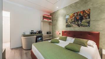Ein modernes Hotelzimmer mit einem großen Bett, grüner Bettwäsche, einem roten Kopfteil, einem Wandbild und einer kleinen Küchenzeile.
