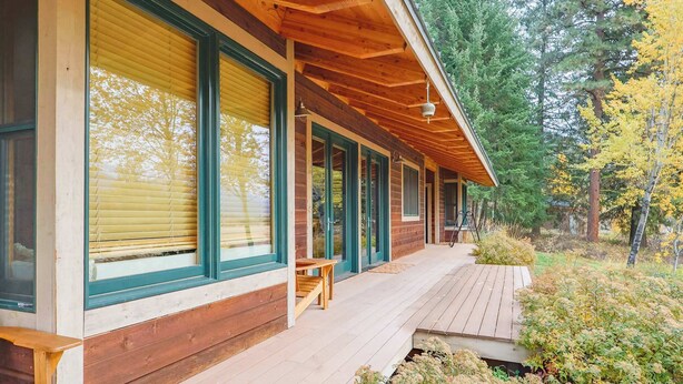 Une cabane en bois dotée de grandes fenêtres, d’un porche et d’une terrasse.