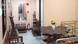 A dining area with a wooden table and chairs, a small statue, and a vase with yellow flowers. - WJV INN BOHOL (Tagbilaran)