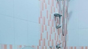 A bathroom with a toilet, a shower, and tiled walls. - WJV INN BOHOL (Tagbilaran)