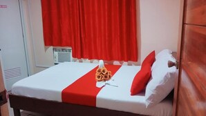 A neatly made bed with a red and white bedspread, a bouquet of sunflowers, and red and white pillows. - WJV INN BOHOL (Tagbilaran)
