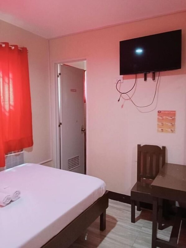 A hotel room with a bed, a desk, a chair, a television mounted on the wall, and a door leading to another room. - WJV INN BOHOL (Tagbilaran)