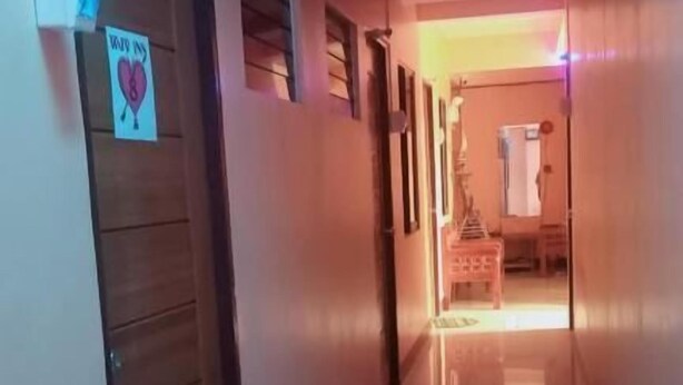 A hallway with a wooden door on the left, a sign with a heart and the number 8, and a glimpse of a room with a bed and a nightstand in the distance. - WJV INN BOHOL (Tagbilaran)