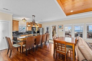 A spacious kitchen with wooden cabinets, a dining area with a large table and chairs, and a view of the city through large windows. - Hot Tub | Beachfront (Crystal Beach)