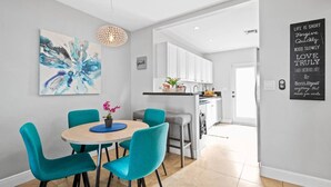Een moderne keuken met witte kasten, een eethoek met turquoise stoelen en een hanglamp.