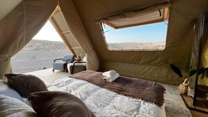 A tented room with a bed, a small table with chairs, and a window overlooking a desert landscape. - Adventurer Camp (Bidiya)