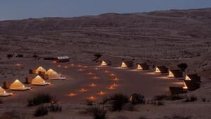 A desert landscape with multiple tents and buildings, some with lights on, suggesting accommodation facilities. - Adventurer Camp (Bidiya)
