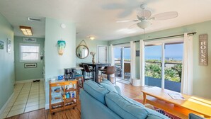 A spacious living room with a large sofa, a dining area, and a balcony with a view of the ocean. - Flagler Beach Escape in the Sun (Flagler Beach)