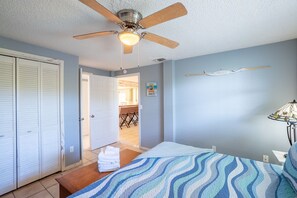 A bedroom with a bed, a ceiling fan, a wall-mounted lamp, and a view of the dining area.