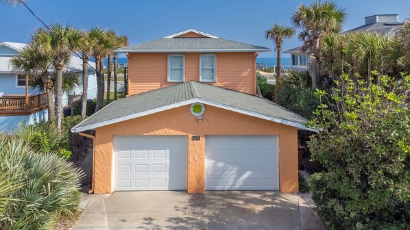 A two-story house with a garage, surrounded by palm trees and a pool.