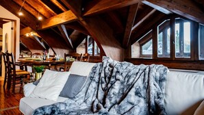 Een gezellige zolderkamer met houten plafond, een eethoek en een bank met plaid.