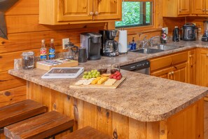 A kitchen with wooden cabinets, granite countertops, a coffee maker, a blender, and a fruit platter. - Epic Private Location*HotTub*FirePit*GameRoom (Pigeon Forge)