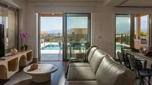 Sala de estar moderna com sofá de couro, mesa de centro e área de jantar com cadeiras. Uma grande porta de vidro deslizante dá acesso a uma área de piscina com vista para montanhas.