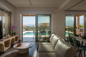 Un saló modern amb un sofà de cuir, una taula de centre i zona de menjador amb cadires. Un gran finestral corredís de vidre dona pas a una zona de piscina amb vistes a les muntanyes.