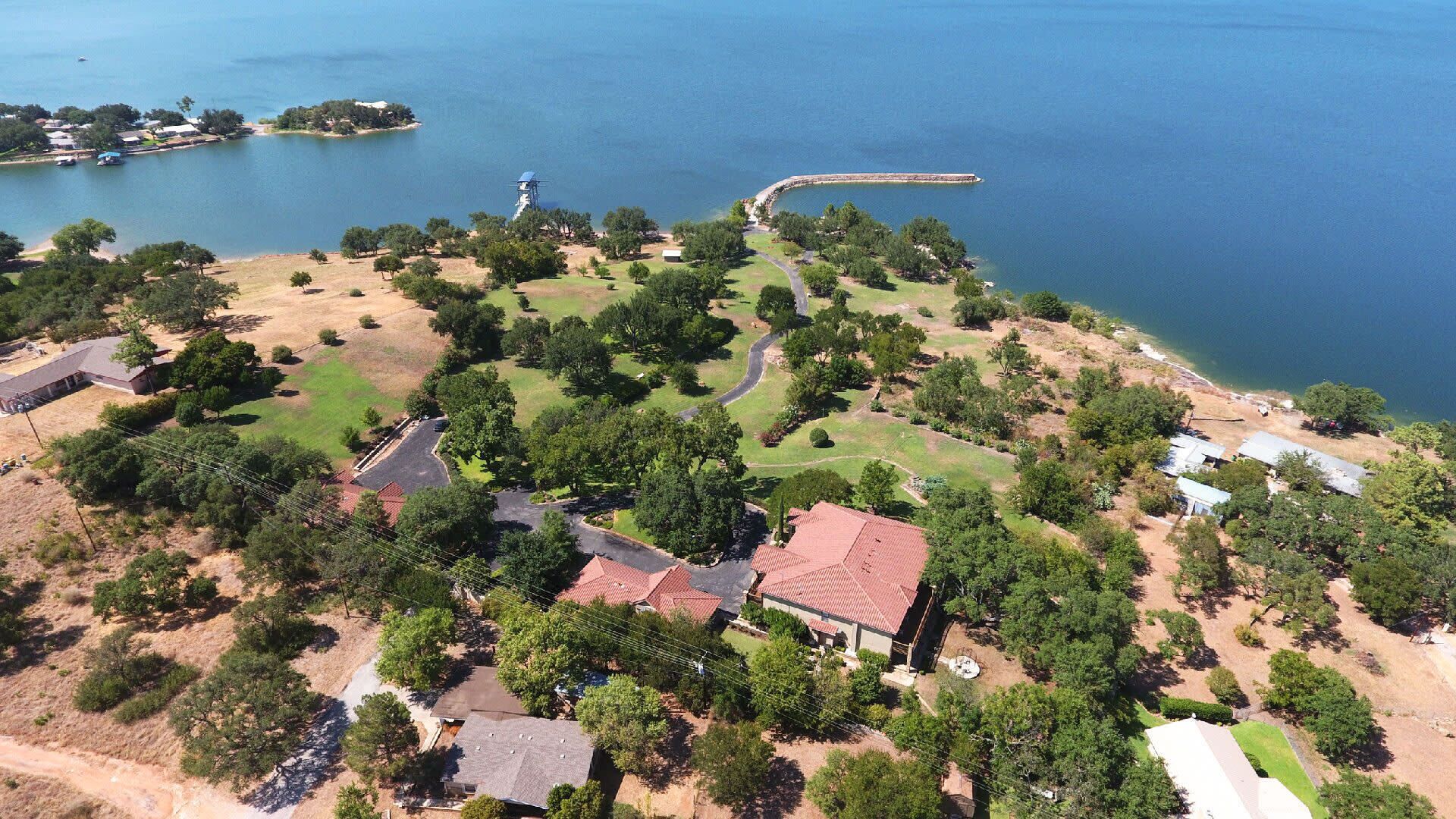 An aerial view of a coastal property with multiple buildings, a winding road, and a body of water.