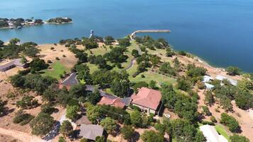 An aerial view of a coastal property with multiple buildings, a winding road, and a body of water.