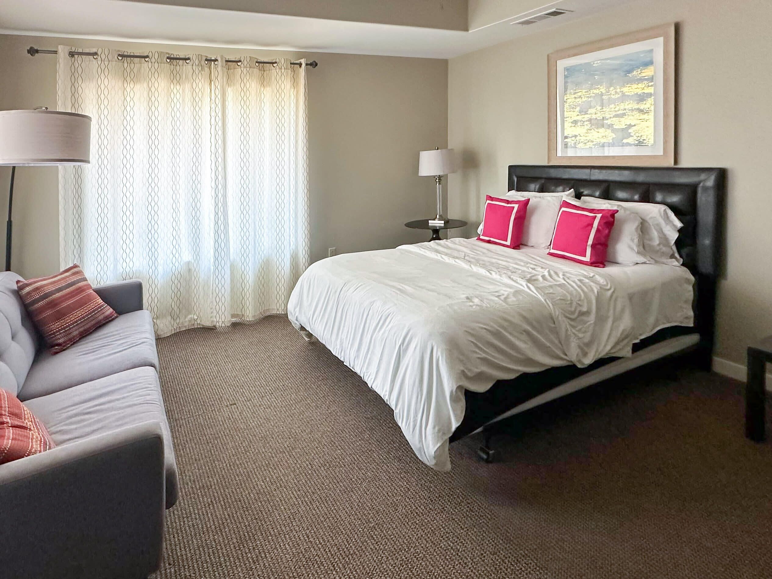 A hotel room with a bed, a sofa, a lamp, and a painting on the wall.