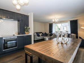 A modern kitchen with dark cabinetry, a wooden dining table, and a built-in oven. - The Willows (Holyhead)