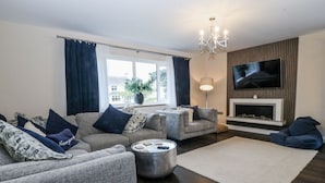 En moderne stue med en hjørnesofa, et sofabord, et fjernsyn ophængt på væggen og en pejs.