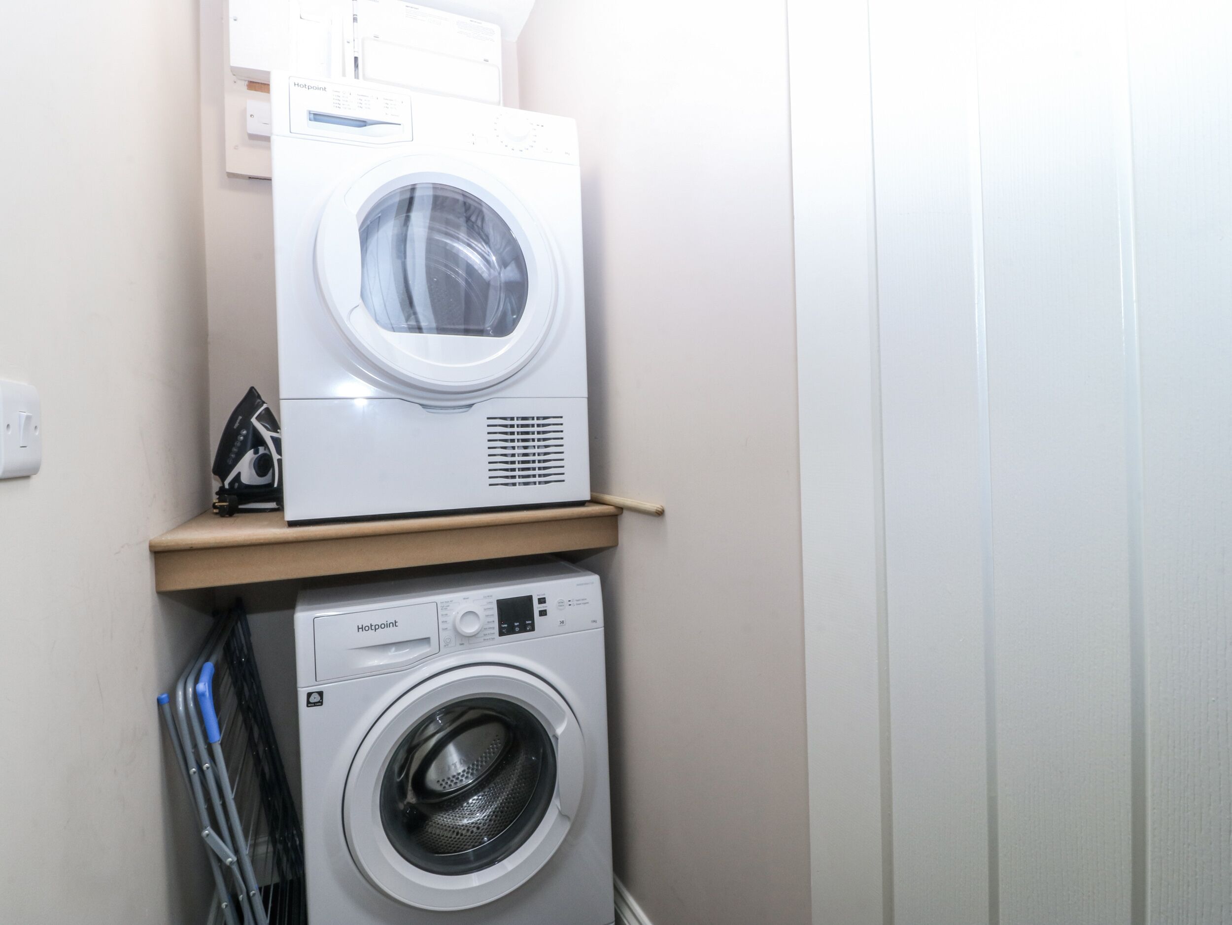 Una zona de bugaderia amb dues rentadores amuntegades sobre una prestatgeria.