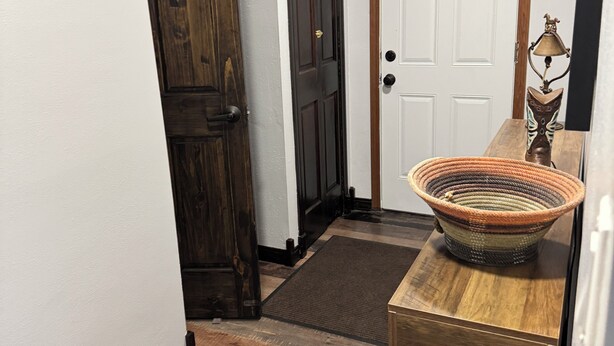 A hallway with a wooden door, a white door, and a small table with a woven basket.