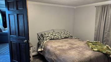A bedroom with a bed, a closed door, a ceiling fan, and a window with curtains.