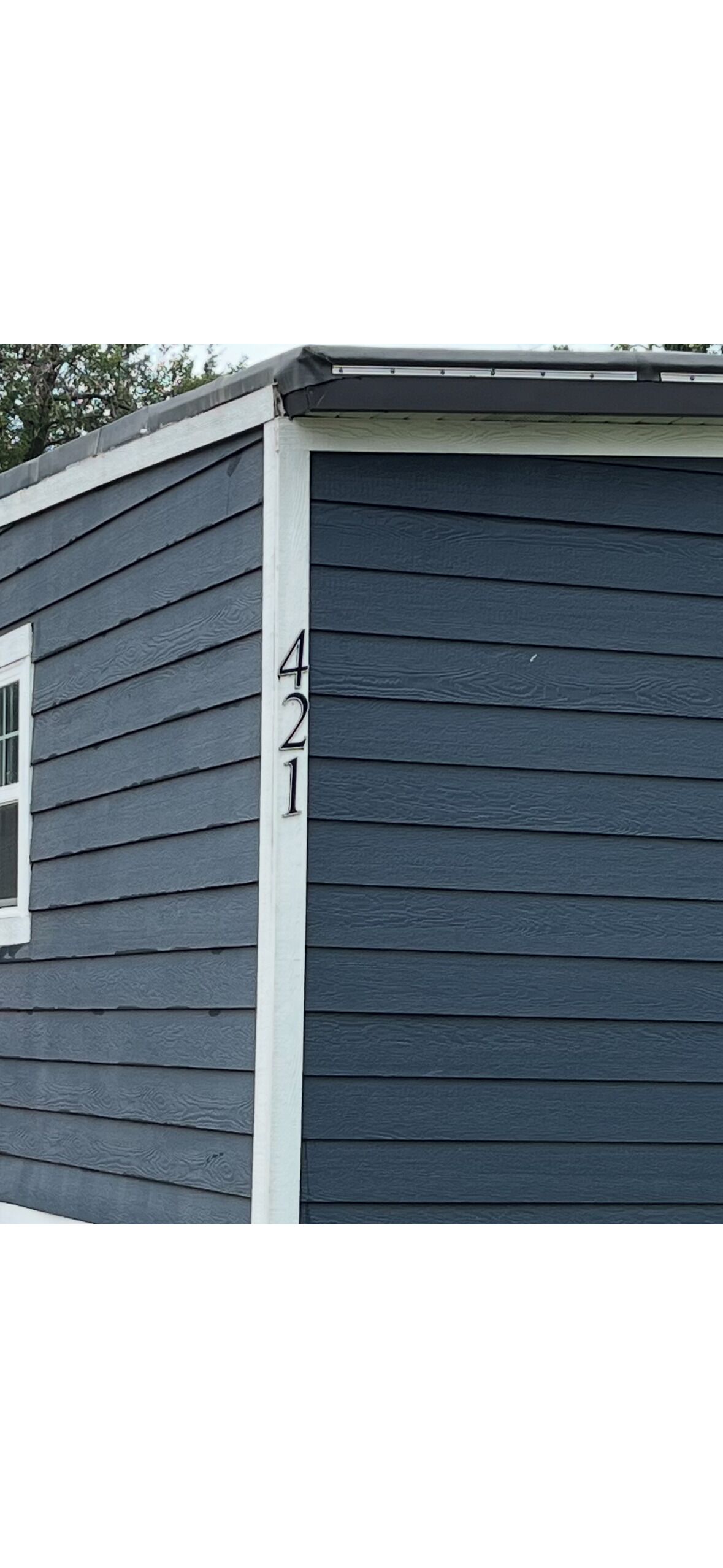 Une maison avec un revêtement extérieur foncé et des bordures blanches autour des fenêtres et de la porte. Le numéro de la maison est le 421.