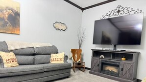 A living room with a grey sofa, a flat-screen TV, a fireplace, and a decorative wall piece.
