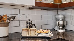Una cocina con armarios blancos, una cafetera, un procesador de alimentos y una bandeja con pasteles.