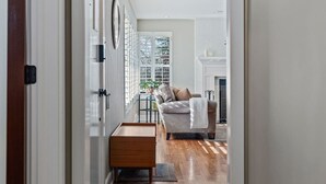 Un pasillo que conduce a una sala de estar con sofá, chimenea y ventana con persianas.