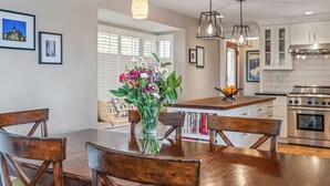 Una cocina moderna con armarios blancos, estufa de acero inoxidable y un comedor con sillas de madera y un florero de vidrio con flores.