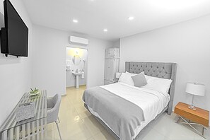 A modern bedroom with a bed, bedside table, chair, and a small desk with a lamp. - Arbol suite (Tijuana)
