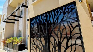 Un bâtiment à la façade beige, une grande porte noire ornée d’un motif représentant un arbre, et une fenêtre située au-dessus de la porte.