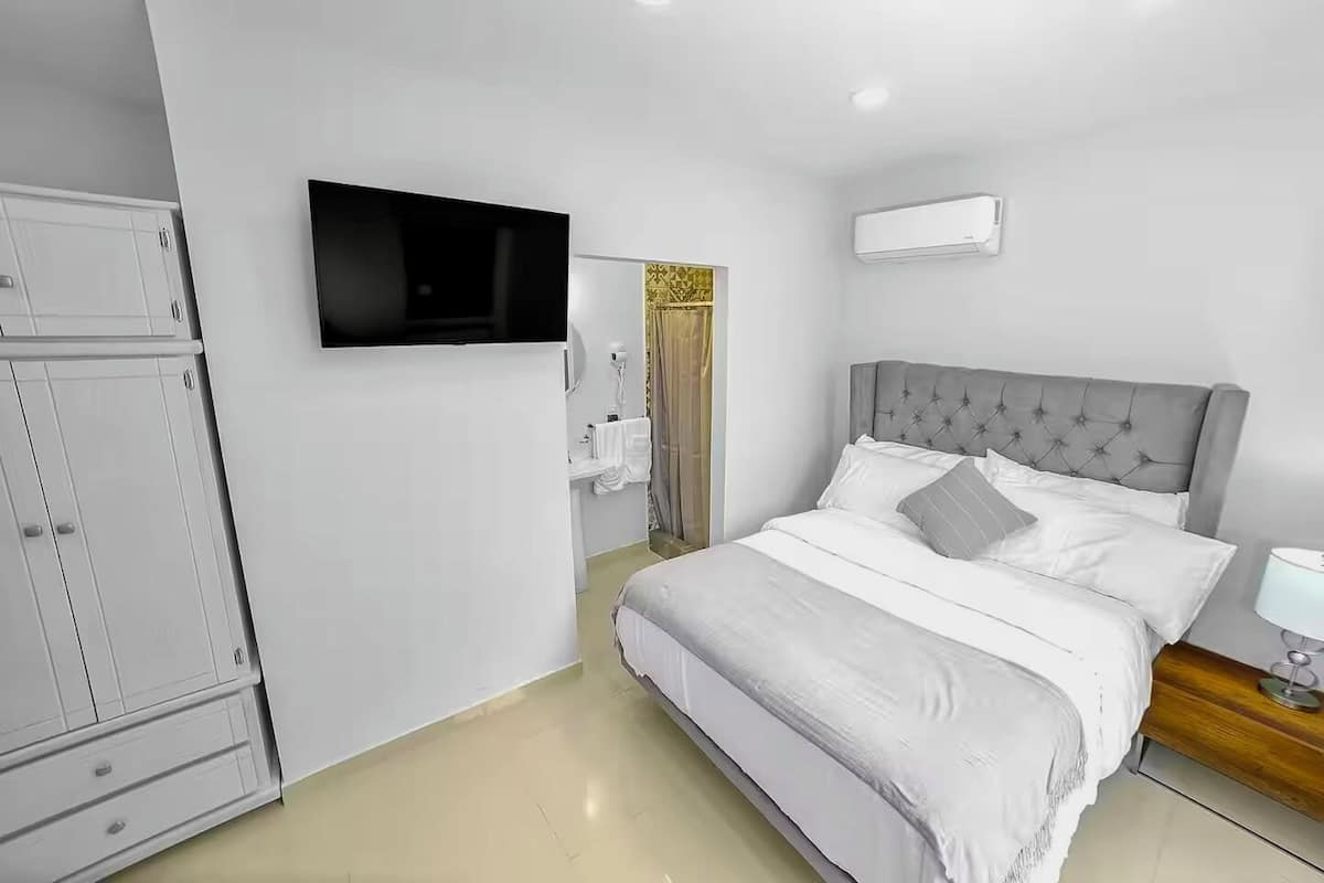 A bedroom with a bed, a wardrobe, a TV, a bedside table, and an air conditioning unit.