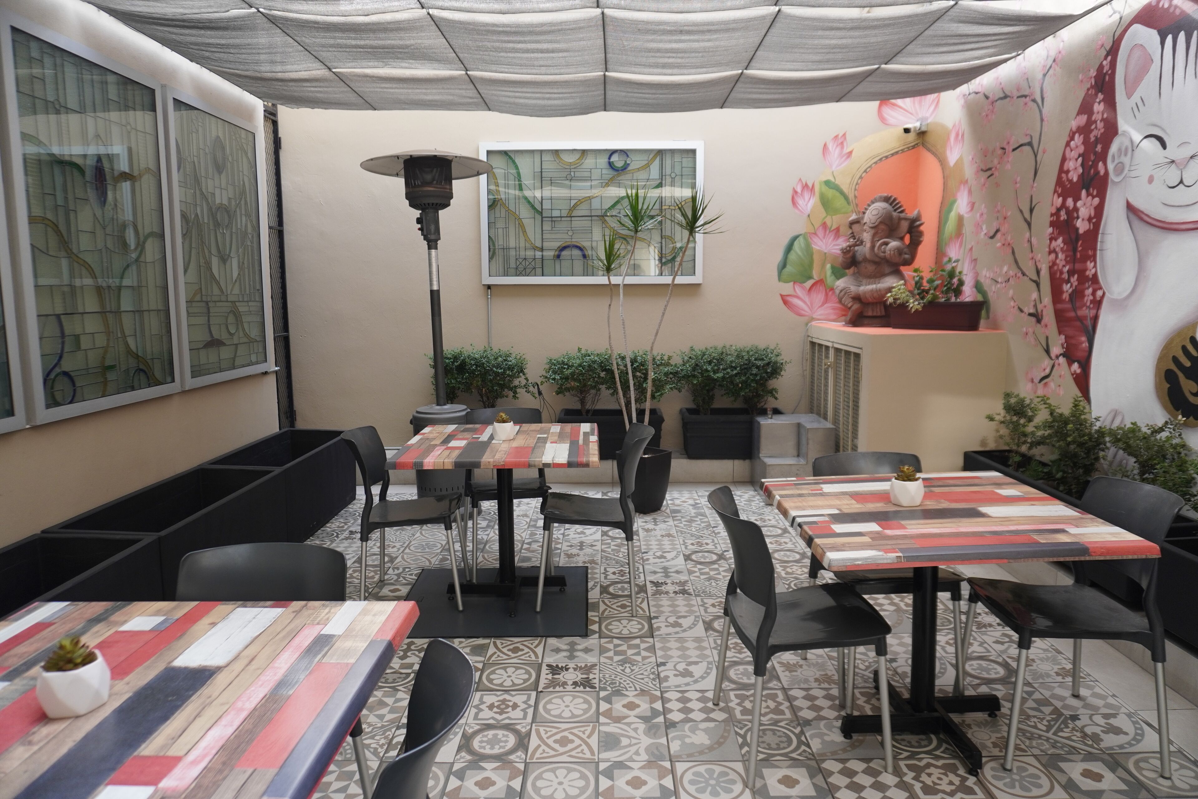 Un restaurant amb diverses taules i caires, decoració mural i plantes en testos.