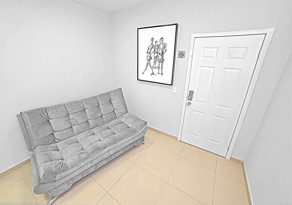 A grey sofa in a room with a white door and a framed black and white drawing on the wall. - Arbol suite (Tijuana)