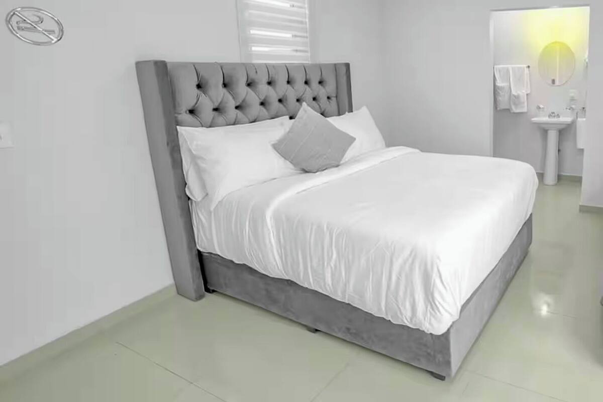 A neatly arranged bedroom with a tufted headboard, white bedding, and a bedside table with a lamp.