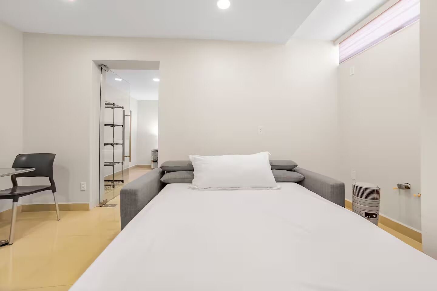Ein schlicht eingerichteter Raum mit einem Bett, einem Sessel und einem kleinen Tisch.
