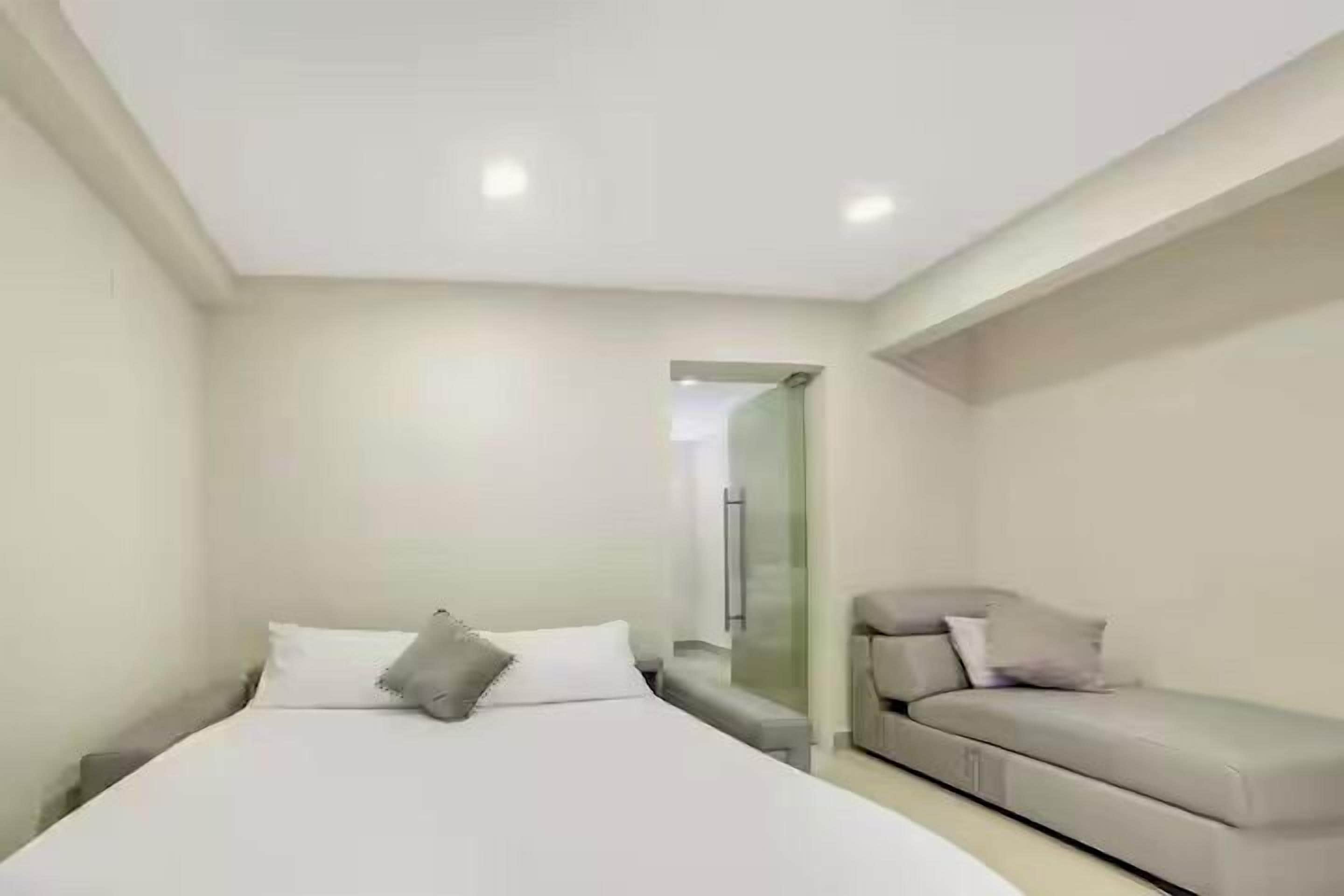Un dormitorio moderno con cama, sofá y mampara de vidrio.