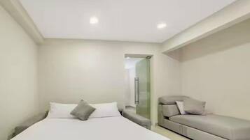 Un dormitorio moderno con cama, sofá y mampara de vidrio.