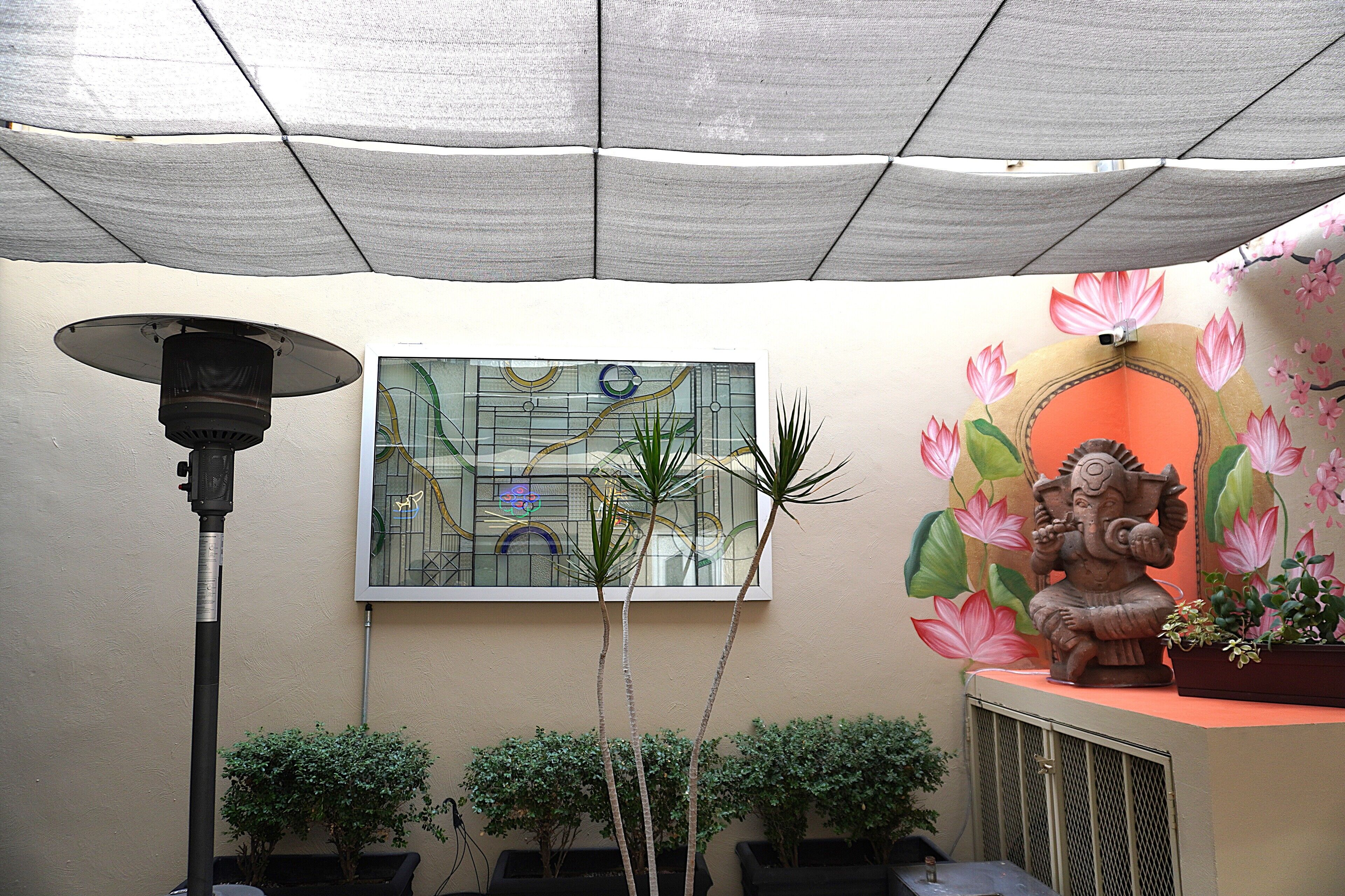 Una habitación con ventilador de techo, planta en maceta, estatua y una ventana de vitral.