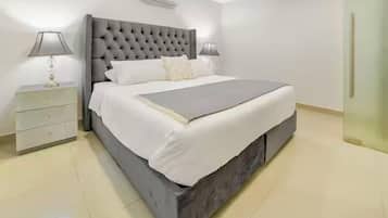 A modern bedroom with a tufted headboard, a large bed with white bedding, two bedside tables with lamps, and a small drawer unit.