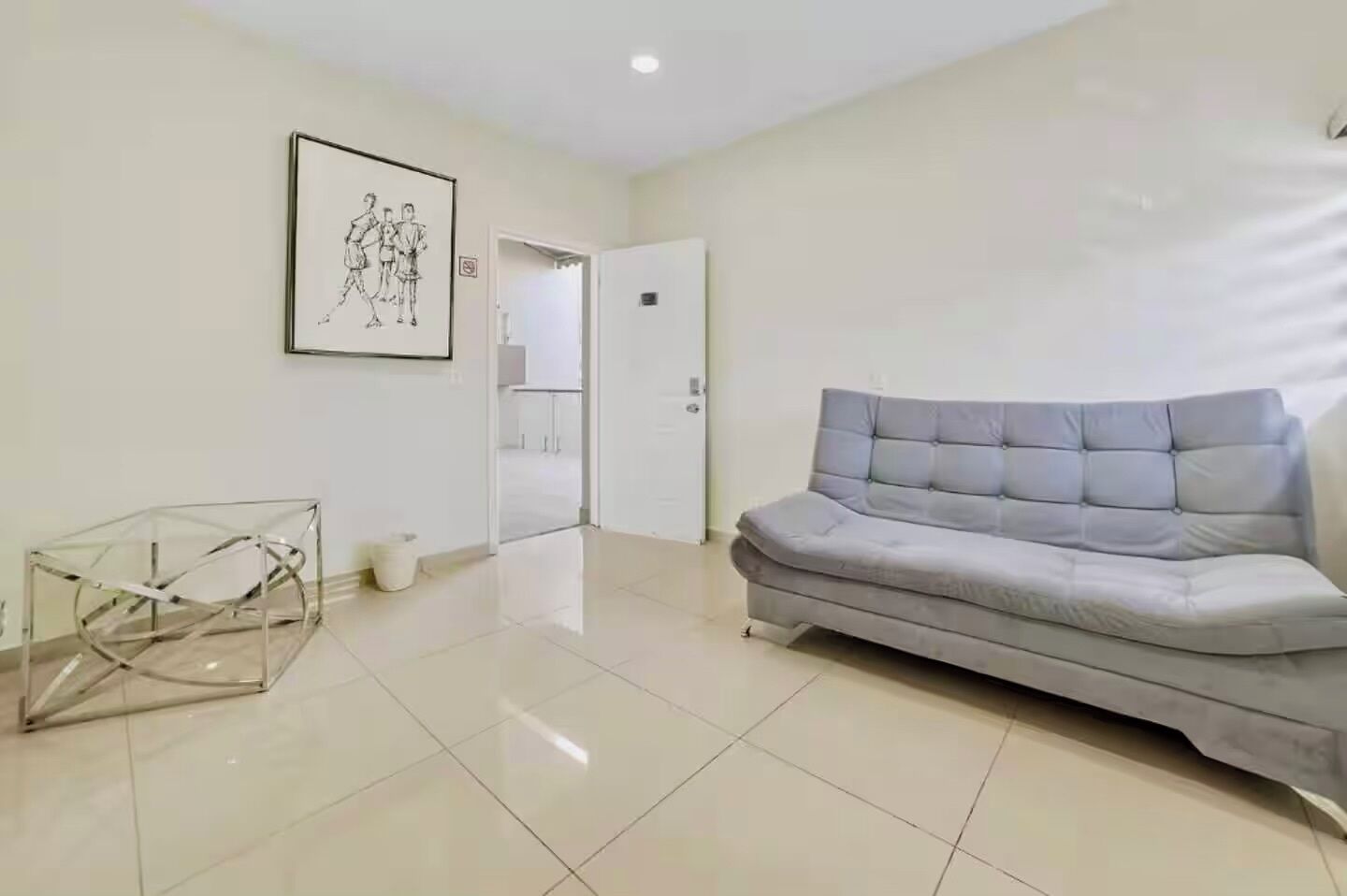 A modern living room with a grey sofa, a glass table, and a framed artwork on the wall.