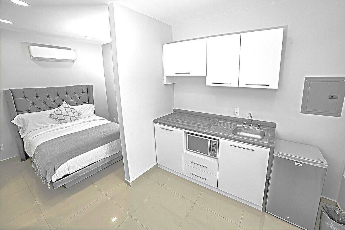 A bedroom with a bed, a small kitchenette with a microwave, and a trash bin.