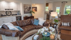 A modern living room with a brown leather sofa, a coffee table with decorative items, and a view of the kitchen and garden. - Classy Country Guest House close to Canton First Monday (Wills Point)
