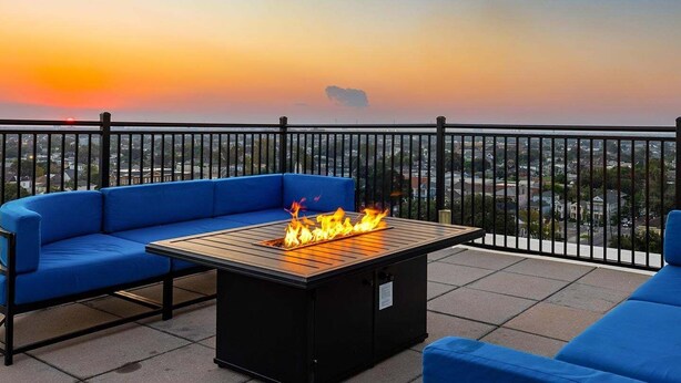Un balcón con una mesa de fuego, asientos acolchados azules y vista a la ciudad al atardecer.