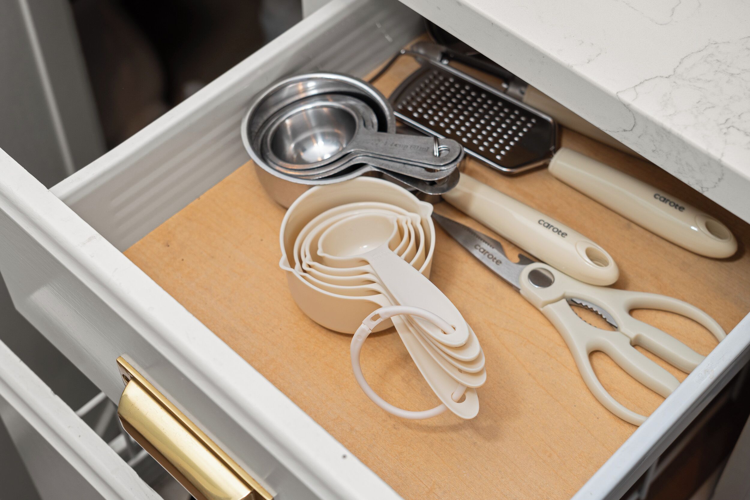 A drawer with measuring tools including a ruler, a grater, and a set of measuring cups.