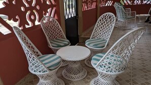 Ein Patio mit weißen Korbmöbeln, darunter Stühle und ein Tisch, auf Fliesenboden.